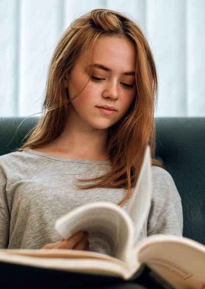 Ginger hair girl with casual clothes reading a book in the library. Sitting relaxed on sofa